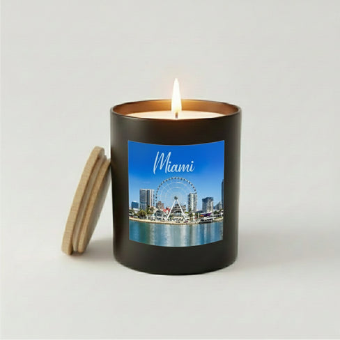 A lit Miami city skyline scented candle in a matte black glass jar with a wooden lid resting alongside.