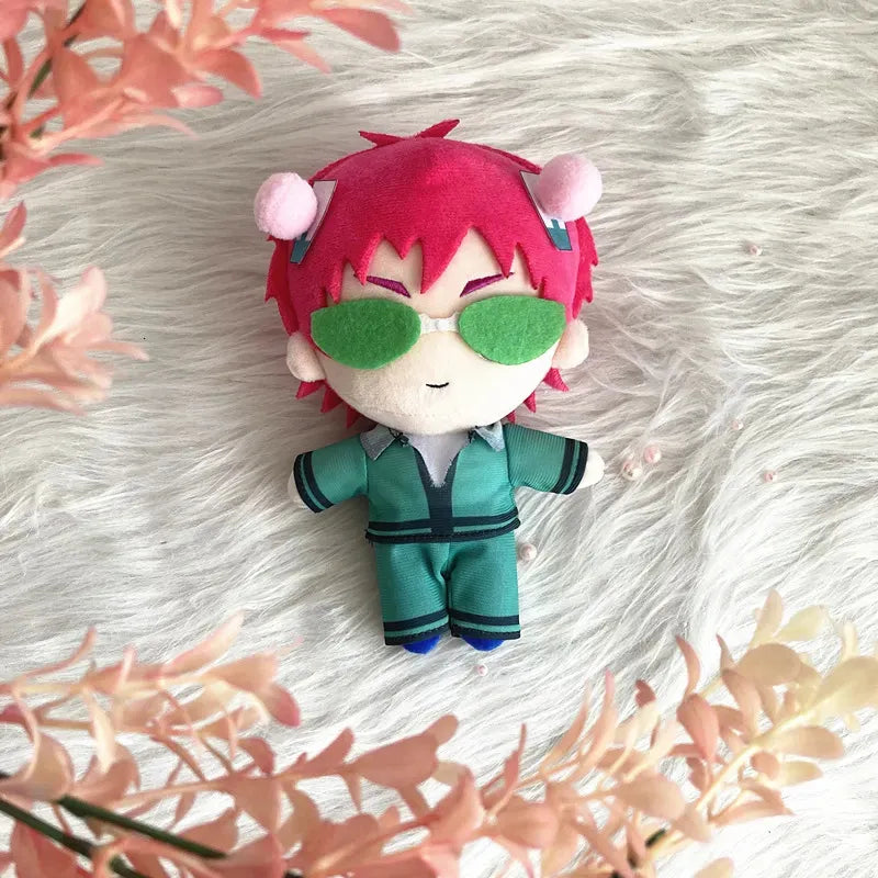 Saiki K Plush toy with red hair and green sunglasses on a fluffy white surface with pink flowers.