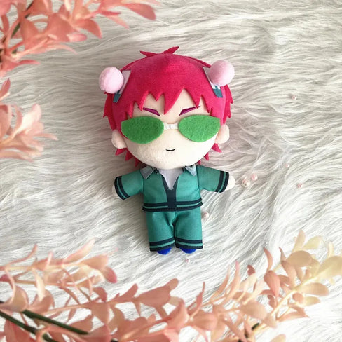 Saiki K Plush toy with red hair and green sunglasses on a fluffy white surface with pink flowers.
