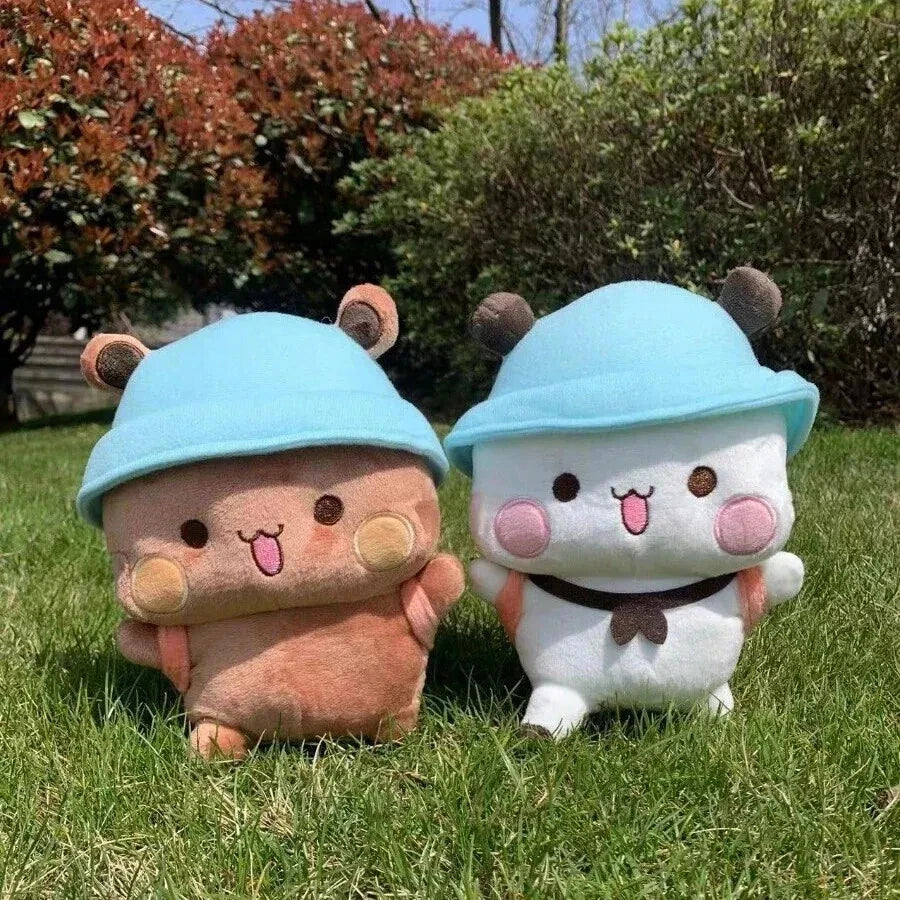 bubu and dudu​ Two plush toys, one pink and one white, wearing blue hats on a grassy background.
