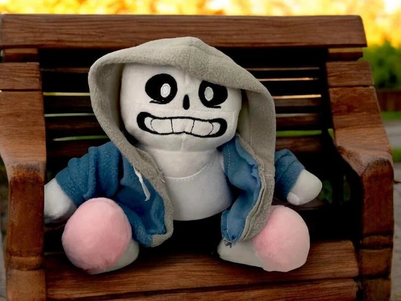 undertale sans plush toy with a hood and blue sleeves sitting on a wooden bench.